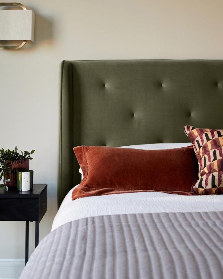 Bedroom featuring a bed with an olive headboard, orange cushion and grey throw, plus a bedside table.