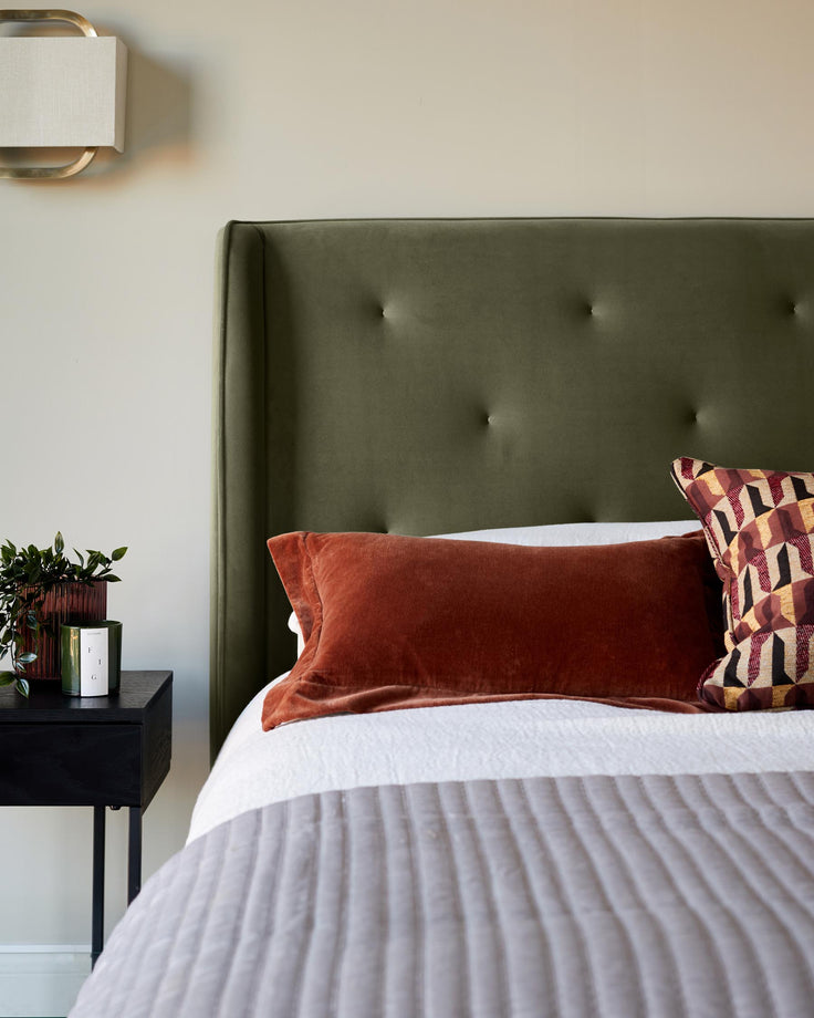 Bedroom featuring a bed with an olive headboard, orange cushion and grey throw, plus a bedside table.