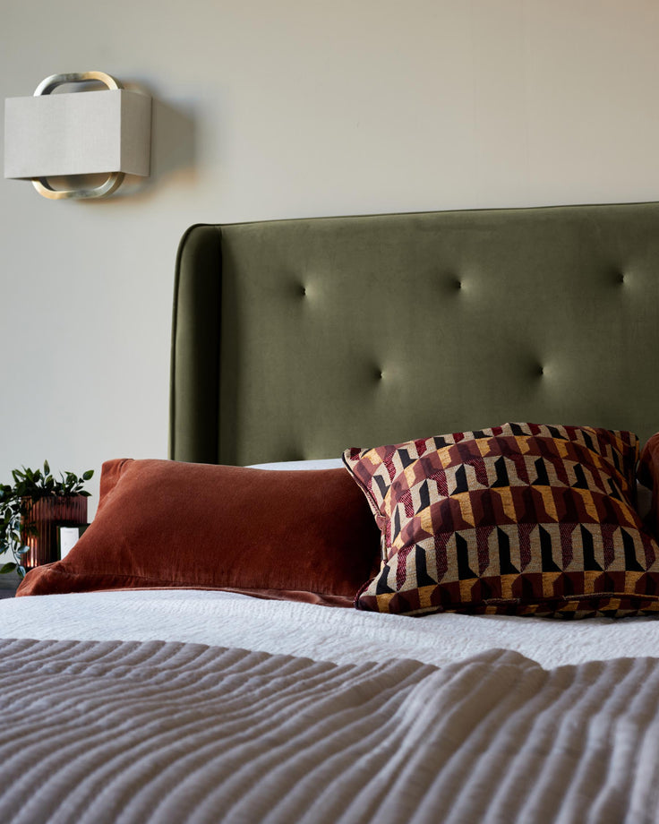 A styled bed featuring an olive headboard, colourful cushions and a textured grey cover.