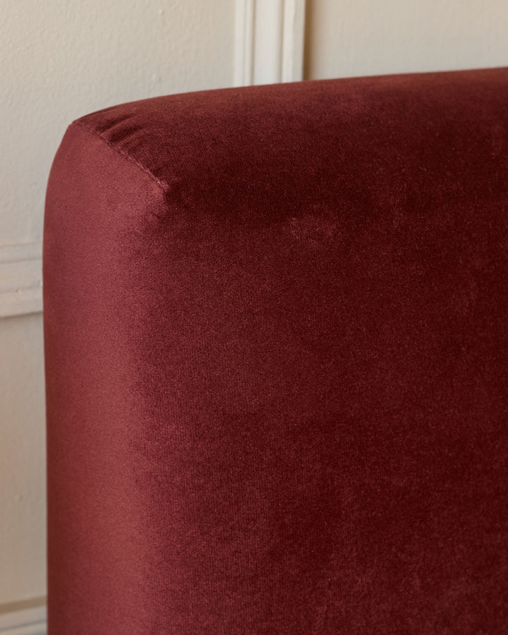 Close-up of a plush, dark red velvet headboard against a neutral wall with classic moulding details.