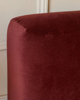 Burgundy velvet ottoman bed with rounded corner detail, close-up side view against neutral wall.