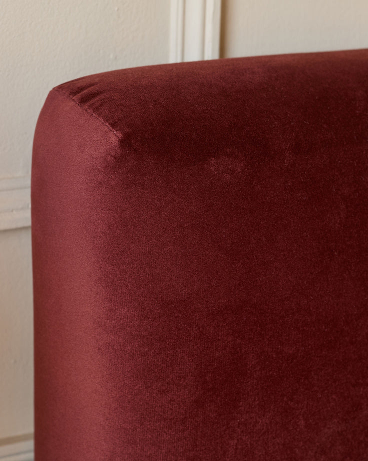 Burgundy velvet ottoman bed with rounded corner detail, close-up side view against neutral wall.