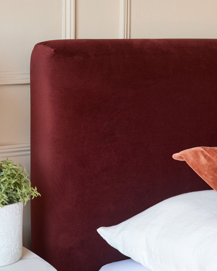 Close-up of a bed headboard in deep red velvet, with a white pillow and bedside table.