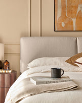 Bedroom furniture including a headboard, bedside table, artwork, mug, & decorative items.