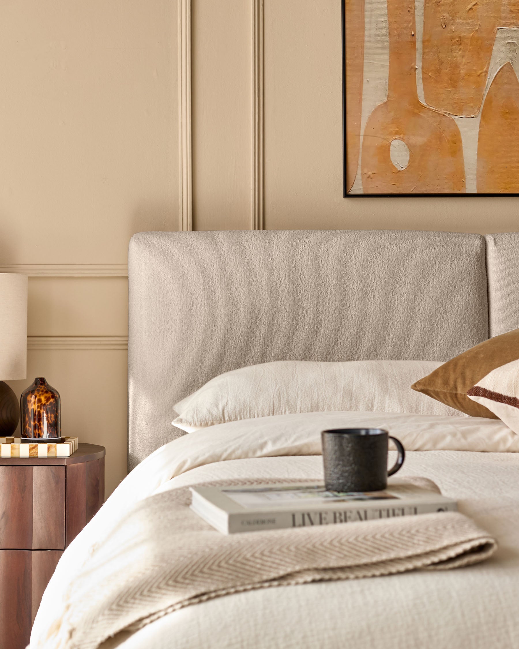 Bedroom furniture including a headboard, bedside table, artwork, mug, & decorative items.