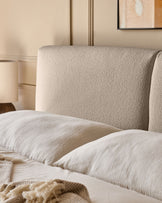 Close-up of a stylish bed with neutral-toned headboard, cushions, and a cosy throw, creating a calming, comfortable bedroom space.