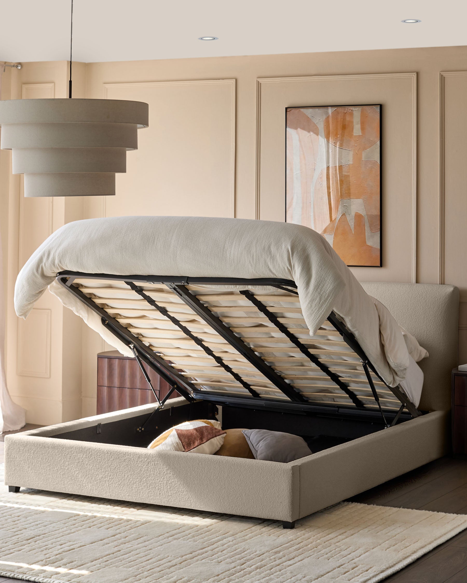 An oatmeal coloured ottoman storage bed with the base lifted up showing storage and cream soft furnishings