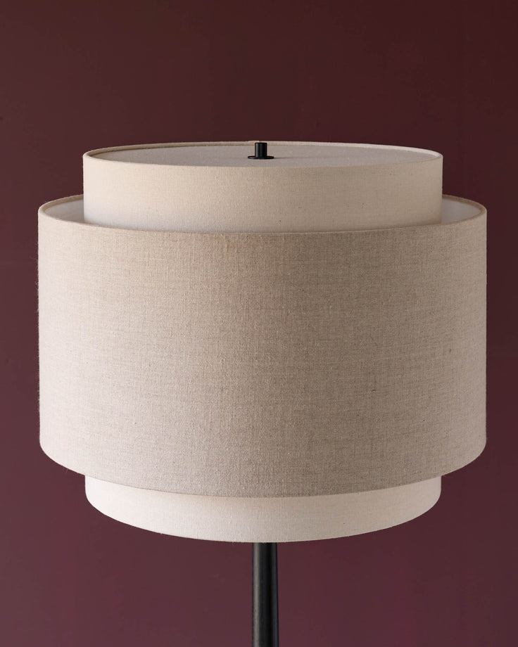 Leonie floor light with tiered cylindrical linen shade in natural and mocha tones against a burgundy background.