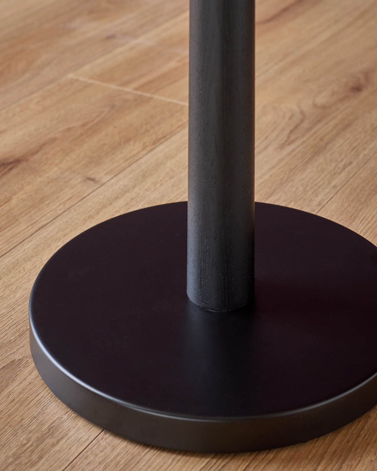 Black floor lamp base with circular weighted foot on wooden floor, vertical pole detail visible.