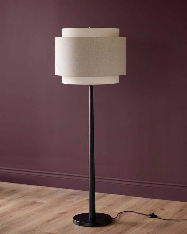 Leonie floor light with layered linen shade in natural and mocha tones, black metal stand and base, against burgundy wall.