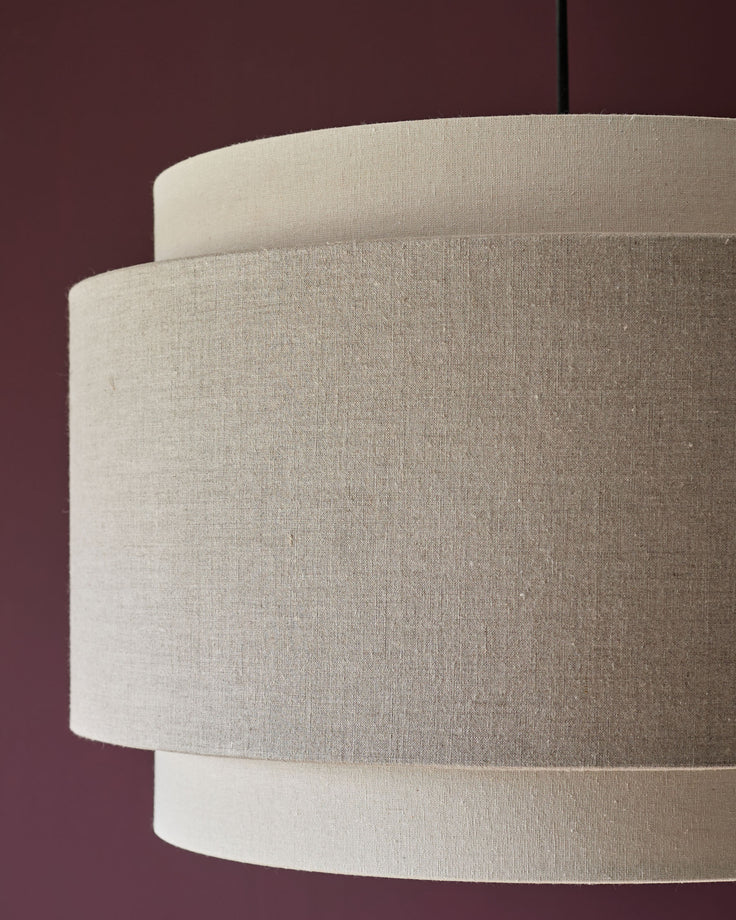 Leonie pendant light with stacked cylindrical linen shades in natural and mocha tones against burgundy background.