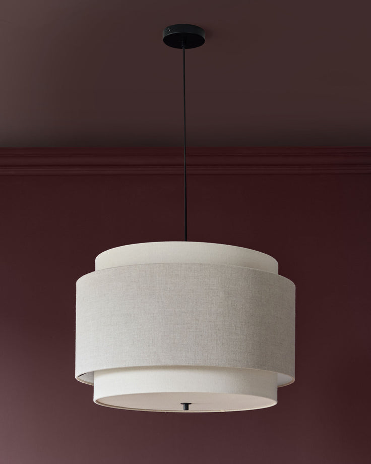 Leonie pendant light with layered cream linen shade and black cord suspension against burgundy wall.