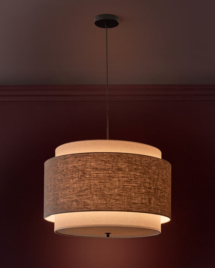 Leonie pendant light with layered drum shade in natural linen and mocha fabric, suspended by black cord from ceiling.