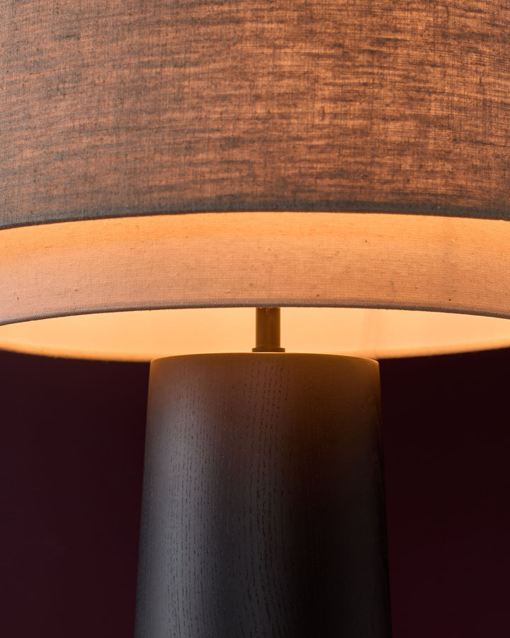Wooden table lamp base with natural linen shade, showing mocha wood grain and warm interior glow.