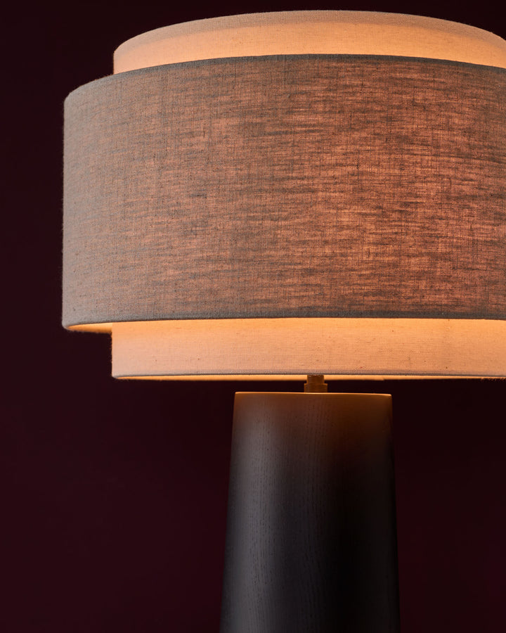 Leonie table lamp with stacked cylindrical linen shades in natural and mocha, dark wood base, lit against dark background.
