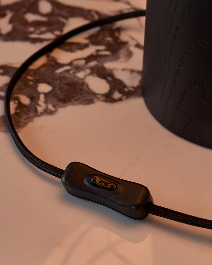 Black fabric cord with inline switch detail on neutral surface, showing table lamp power control mechanism.