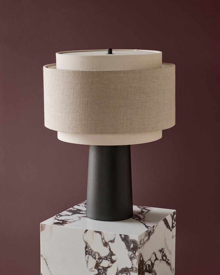 Leonie table lamp with natural linen shade, dark wood stem, and marble base against mauve background.