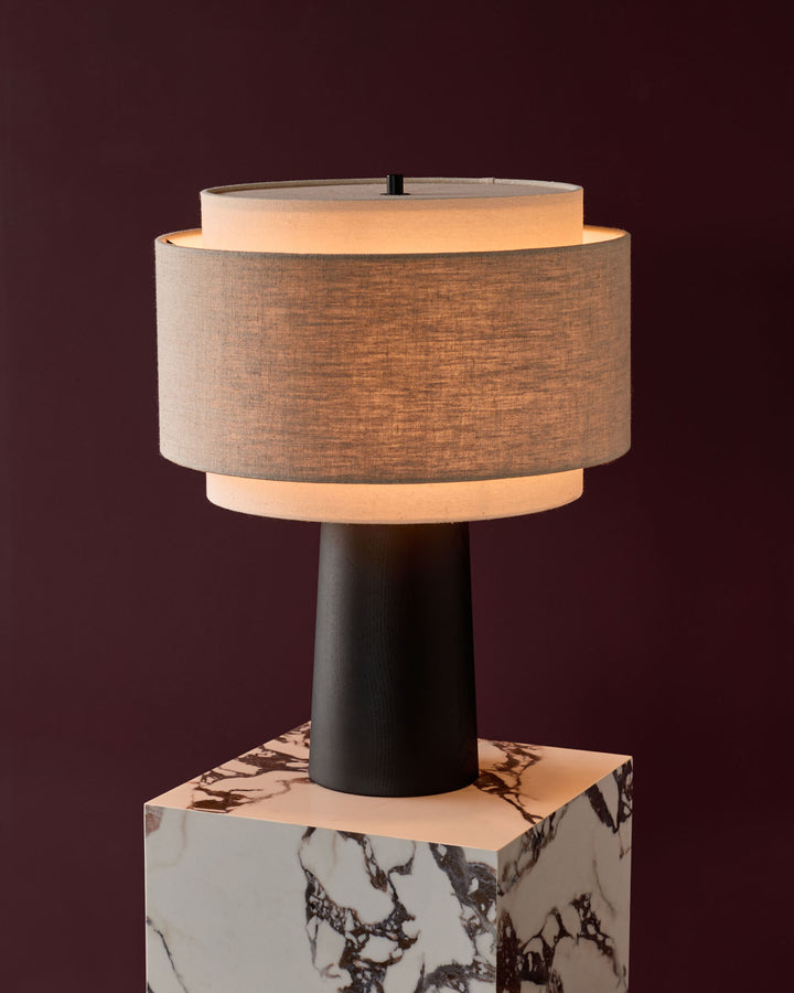 Leonie table lamp with natural linen shade, mocha trim, dark wooden base, and marble base on burgundy background.
