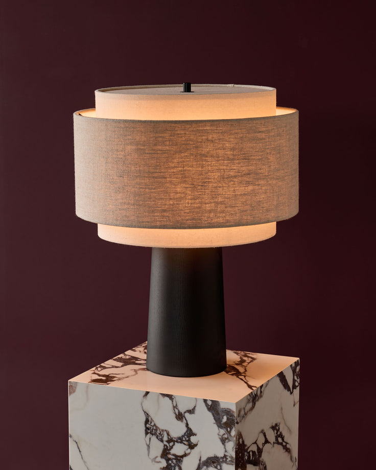 Leonie table lamp with natural linen shade, mocha trim, dark wooden base, and marble base on burgundy background.