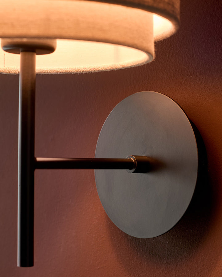 Leonie wall light with natural linen shade and mocha metal accents, showing circular backplate detail.