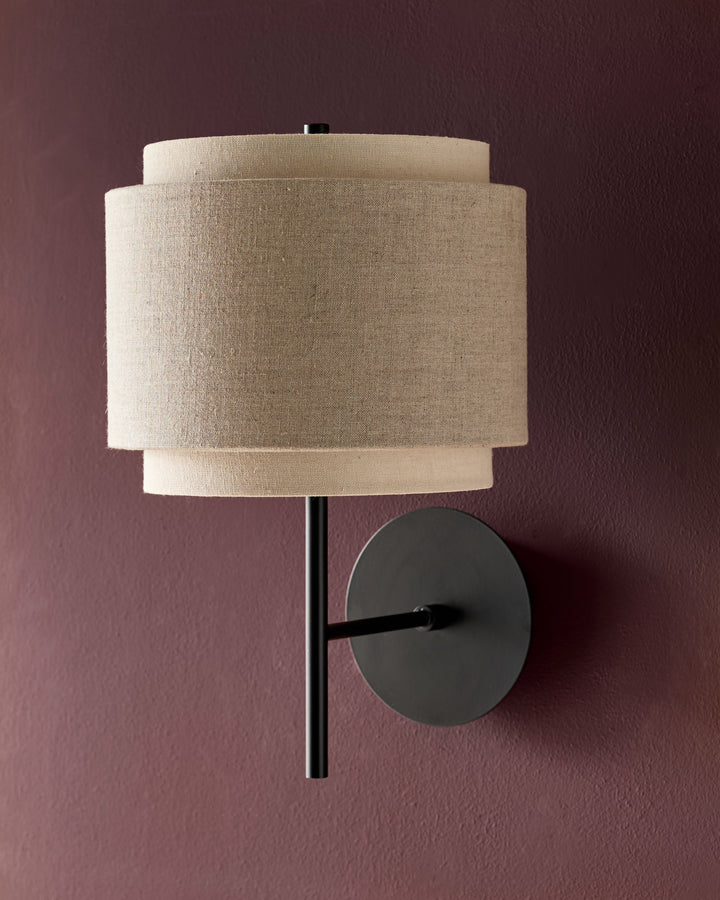 Leonie wall light with natural linen shade and mocha metal fixture mounted on mauve wall.