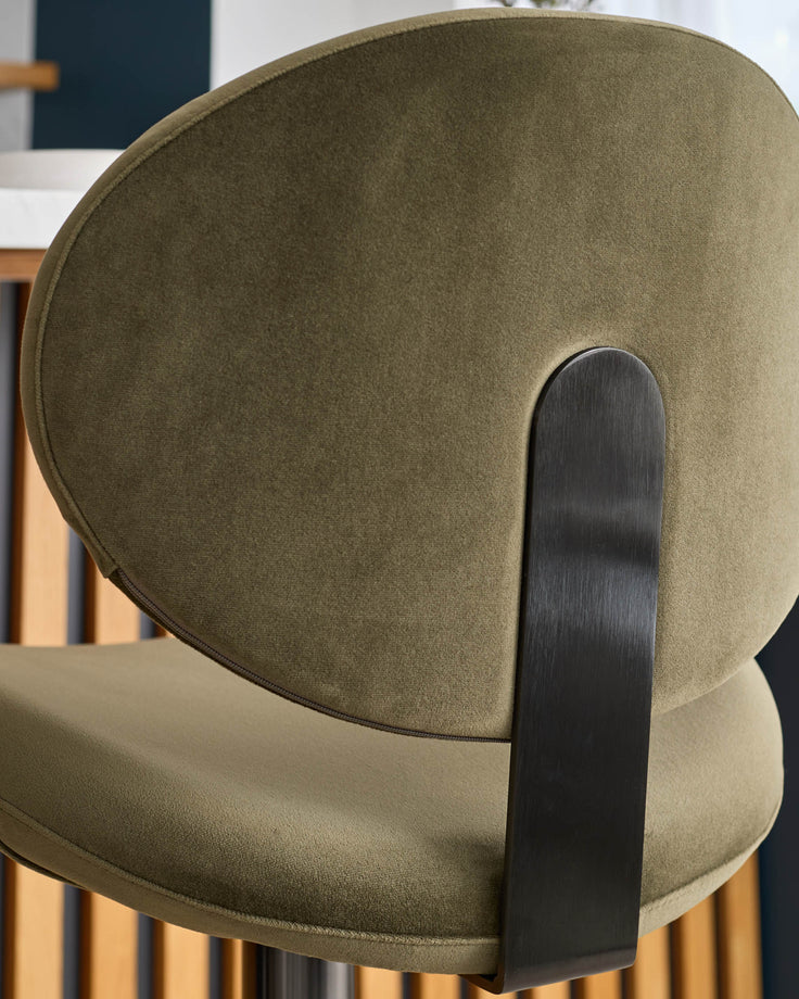 Olive green velvet bar stool with curved backrest and black metal handle, side view.
