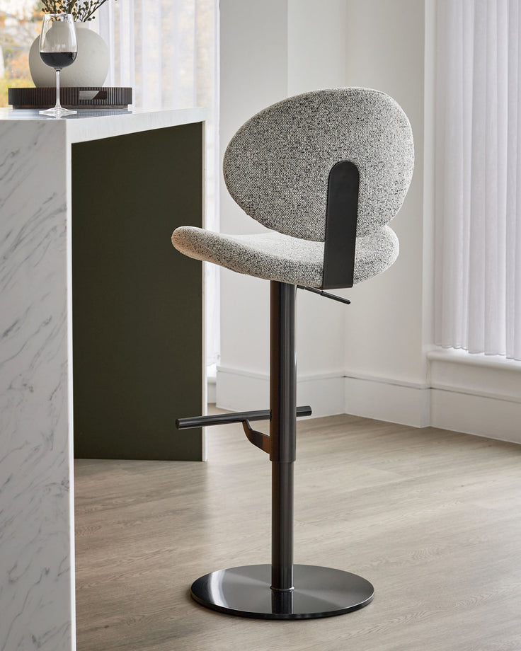 Lilah grey fabric gas-lift bar stool with rounded backrest, black metal frame and base, shown in modern kitchen setting.