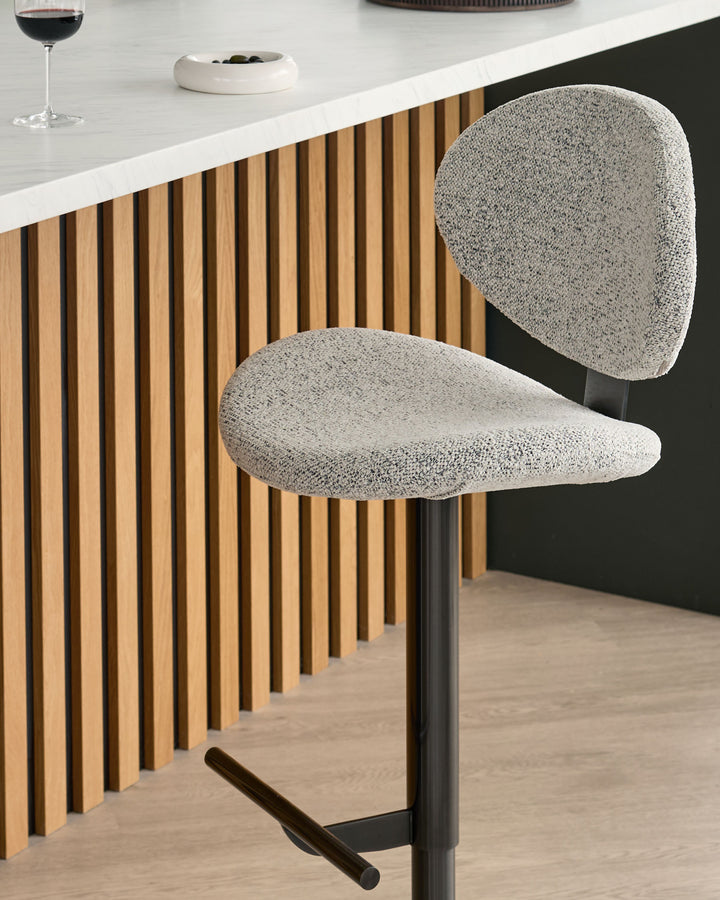 Lilah grey fabric bar stool with rounded backrest and black metal base, shown at kitchen counter.