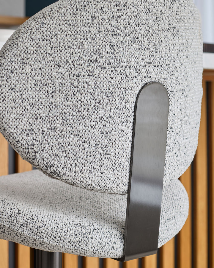 Lilah gas lift bar stool in grey fabric with curved backrest and brushed metal handle detail, side view.