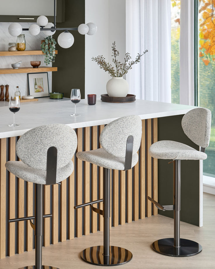 Lilah gas lift bar stool in grey fabric with curved backrest, chrome pedestal base, and footrest at a kitchen island.