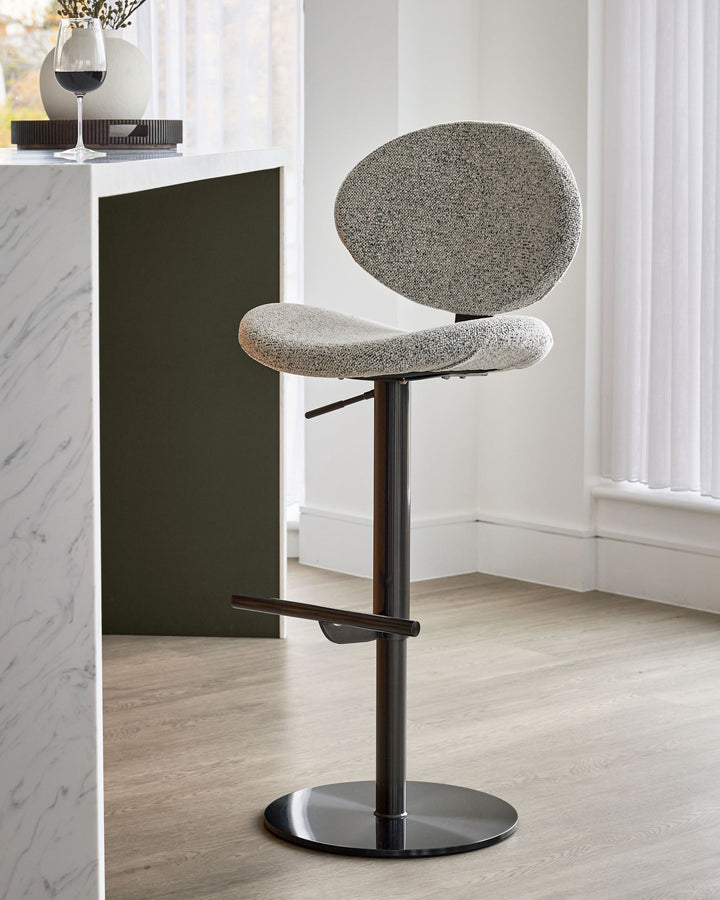 Lilah grey fabric bar stool with round backrest, curved seat, black metal base and footrest, adjustable height.