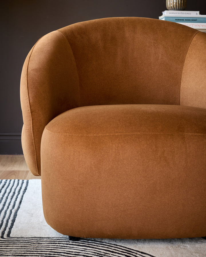Lillian accent chair in caramel fabric, shown from a side angle displaying its curved rounded silhouette and plush upholstery.