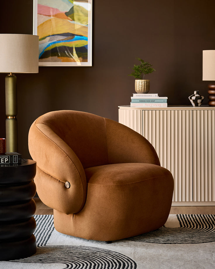 Lillian accent chair in caramel fabric with curved, rounded shape and button detail, shown in styled living room setting.