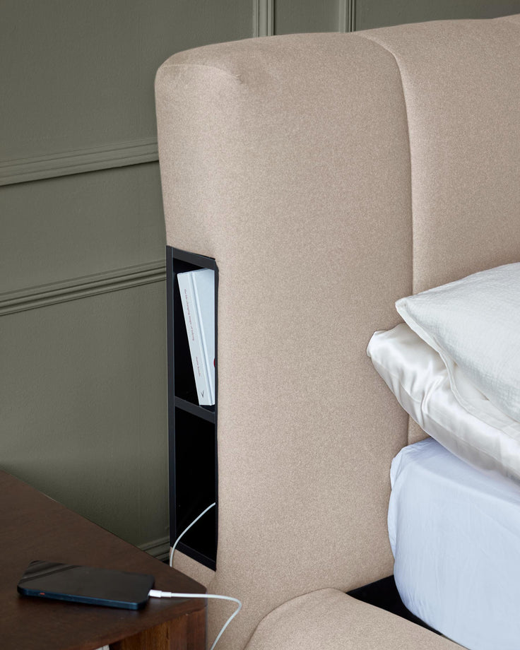 Close-up of a stylish bed with built-in storage. Includes shelving in the headboard and a bedside table with phone charging.