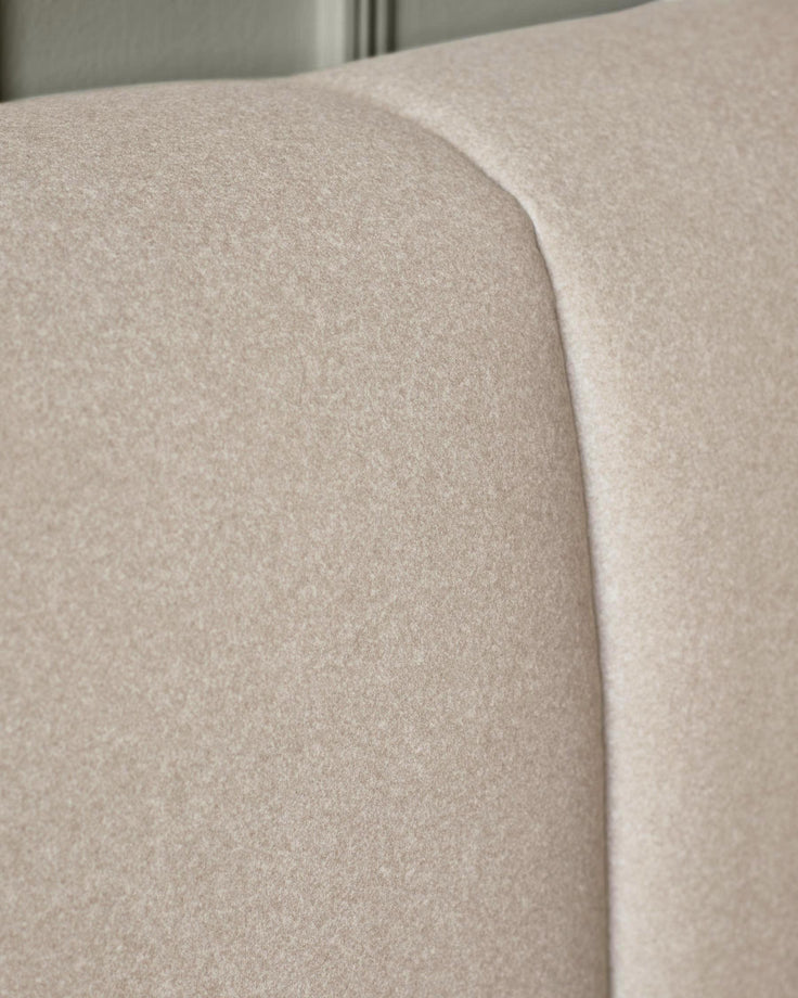 Close-up of a neutral coloured, upholstered headboard, showing texture and subtle curves.