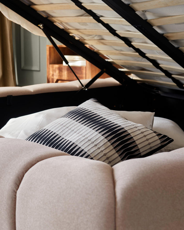 Close-up of a bed with a striped cushion and lift-up frame, revealing storage space.