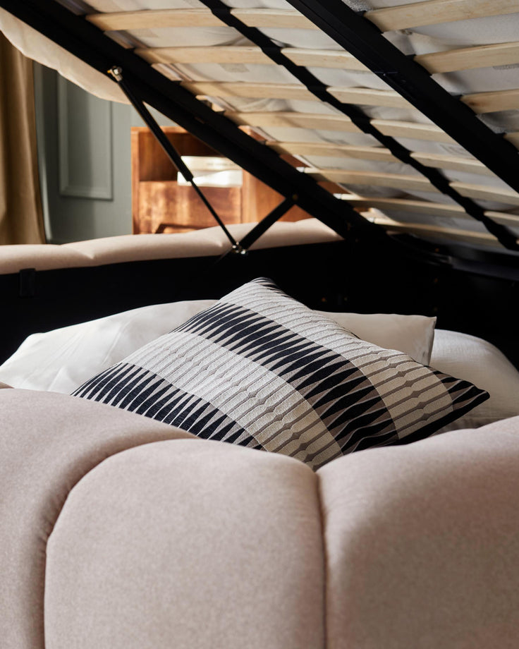 Close-up of a bed with a striped cushion and lift-up frame, revealing storage space.