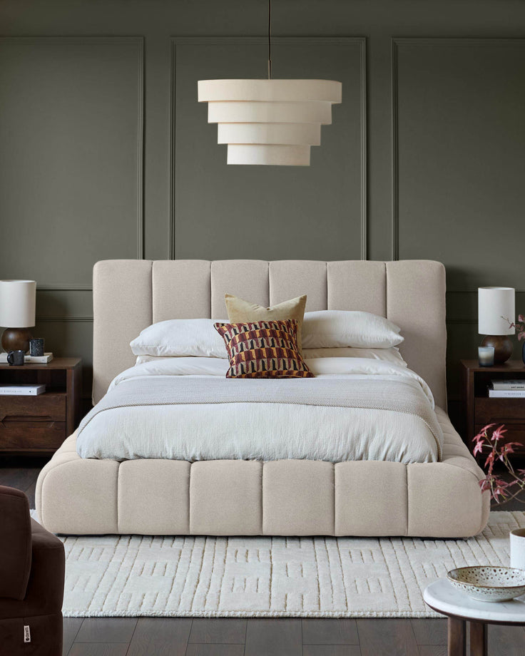 A neutral-toned bedroom features a panelled bed, bedside tables, lamps, a tiered pendant light, and a textured rug.