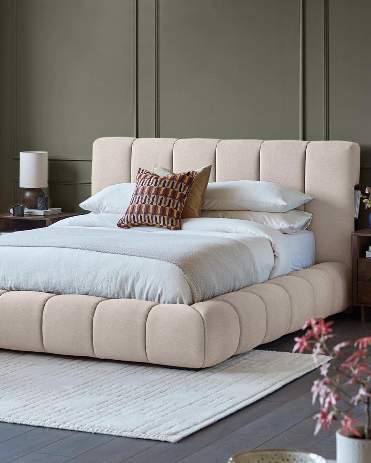 A padded beige platform bed with matching headboard, accessorised with patterned cushions and a cosy throw.