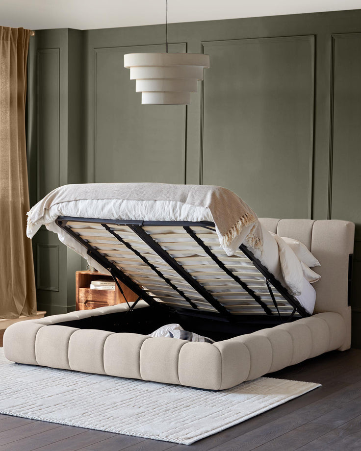 Upholstered ottoman storage bed in neutral fabric, with wooden floors and a layered pendant light.