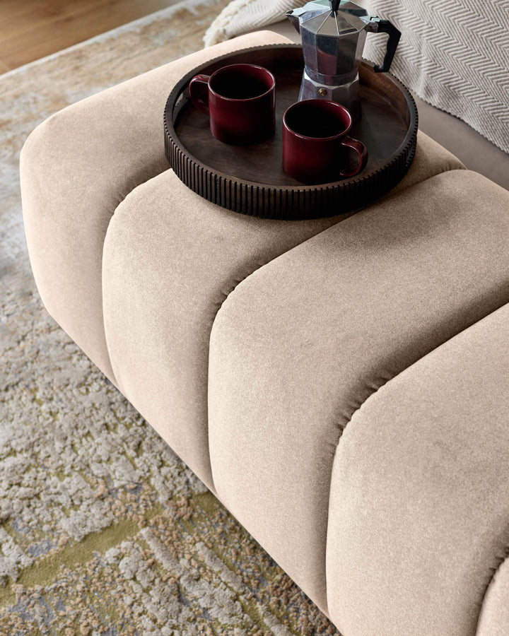 Cream fabric bench with curved channeled design, styled with dark round tray holding two burgundy mugs and moka pot.