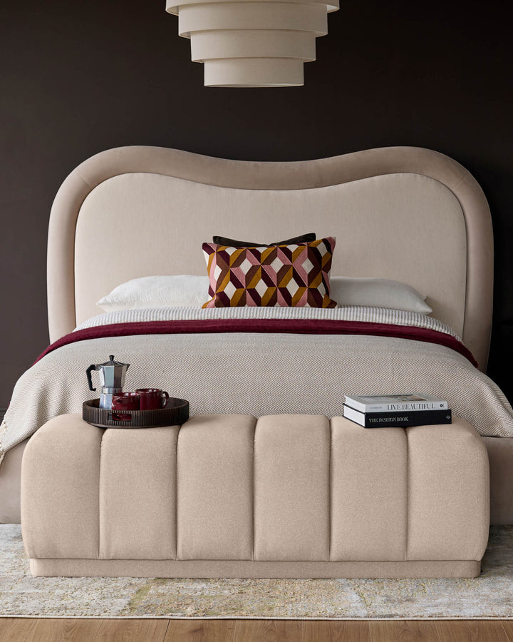 Cream fabric bench with vertical channel quilting, positioned at foot of upholstered bed in styled bedroom setting.
