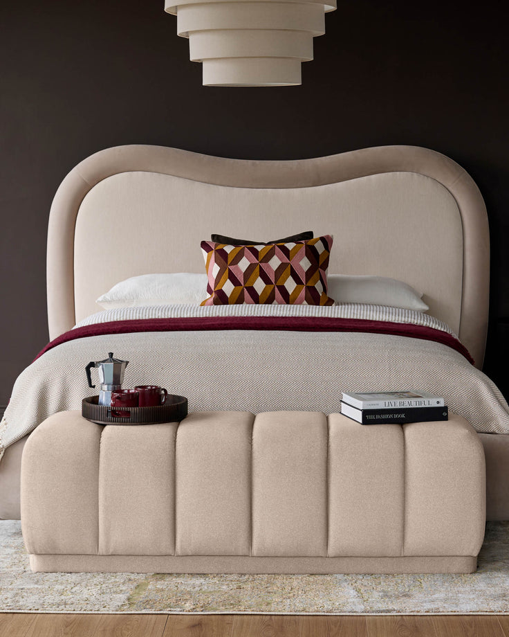 Cream fabric bench with vertical channel quilting, positioned at foot of upholstered bed in styled bedroom setting.
