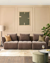 Modular brown sofa with cushions, coffee table and ottoman, sitting on a light rug and dark wooden floor.