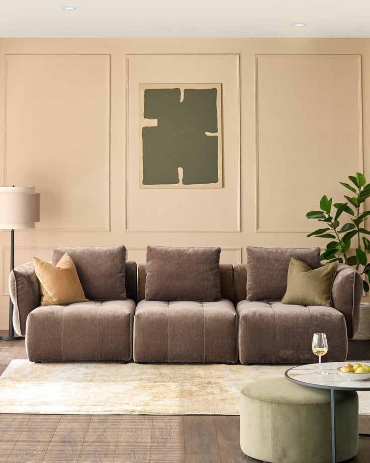 Modular brown sofa with cushions, coffee table and ottoman, sitting on a light rug and dark wooden floor.
