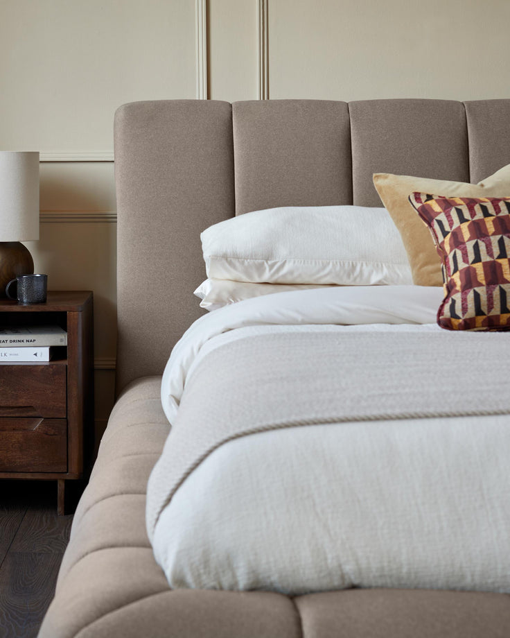 Bedroom featuring a bed with a neutral coloured upholstered headboard, side table and soft furnishings.
