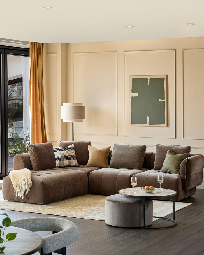 A modern, brown sectional sofa with a round coffee table, ottoman, and various throw pillows. Stylish interior design.