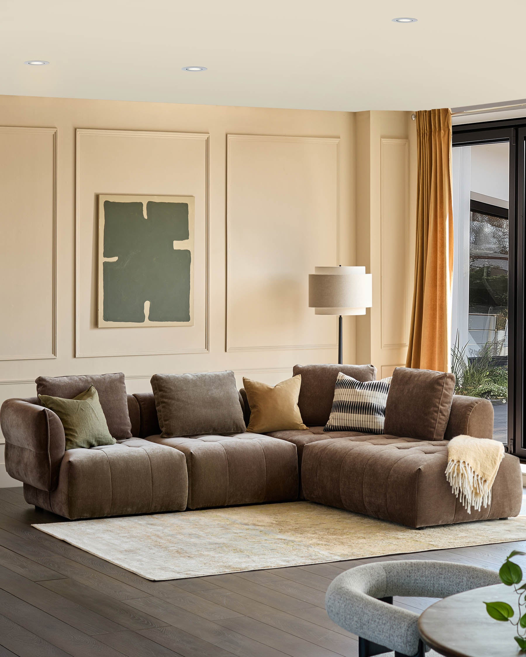 A stylish living room featuring a modular brown sofa adorned with cushions, a patterned rug, and a floor lamp.
