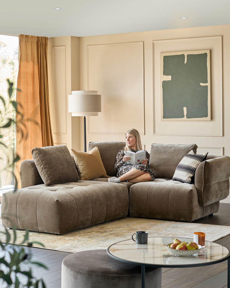 Stylish living room with a comfy L-shaped sofa, round coffee table and reading woman creating a relaxed atmosphere.