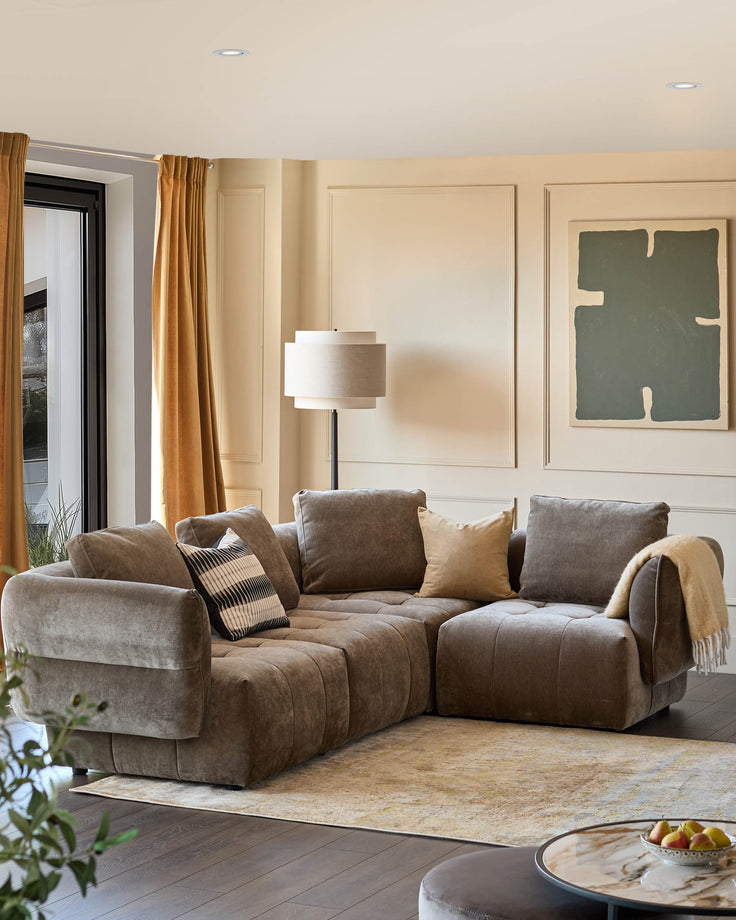 A comfy corner sofa in a neutral room with a floor lamp, marble table, rug and abstract art. Perfect for lounging!